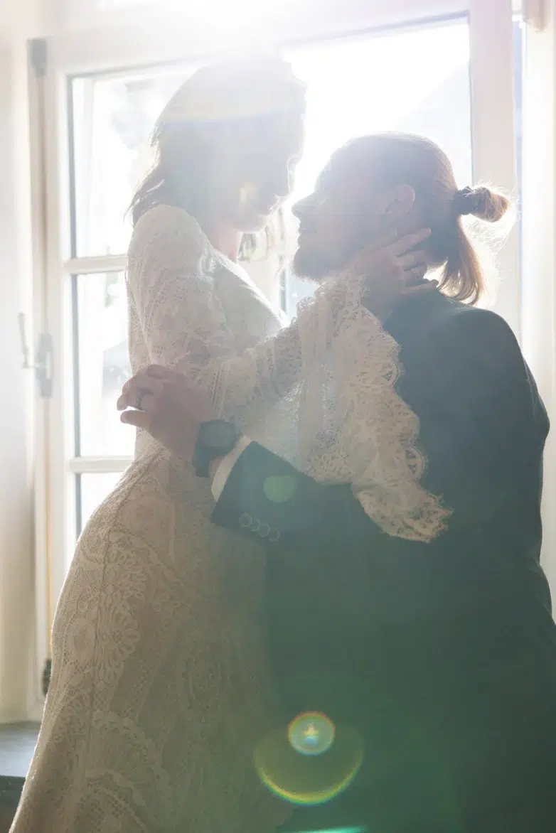 Bride and groom embracing in backlit window light at Château d'Urspelt, Clervaux, Luxembourg.