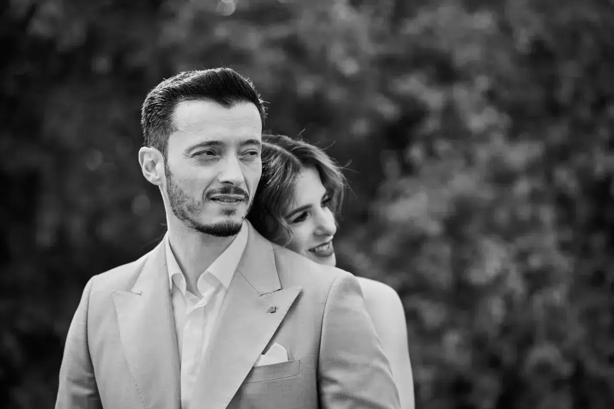 Candid black and white photo of a groom and bride sharing a quiet smile in a park setting on their wedding day in Luxembourg.