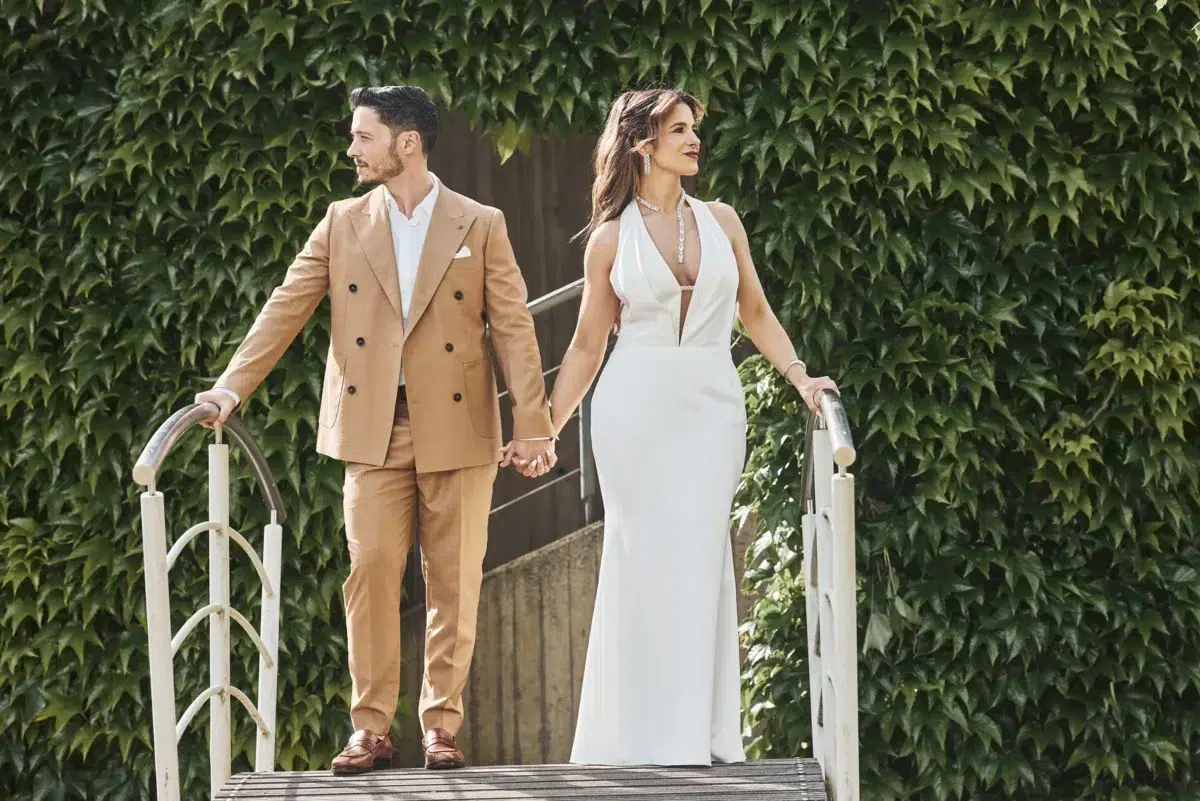 Newlyweds walk hand in hand across a small bridge framed by ivy, a romantic moment from their Luxembourg wedding day.