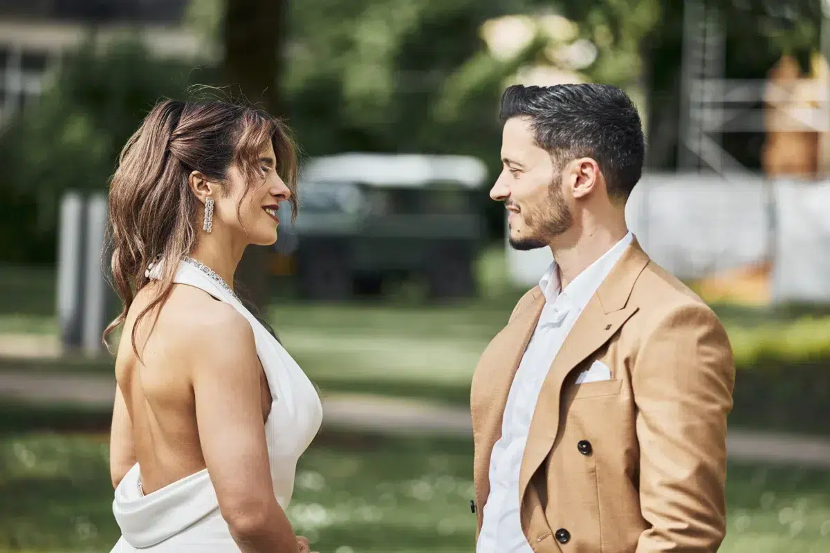 Bride and groom stand nose to nose in profile, a tender moment captured in the park with a vintage Land Rover in the background.