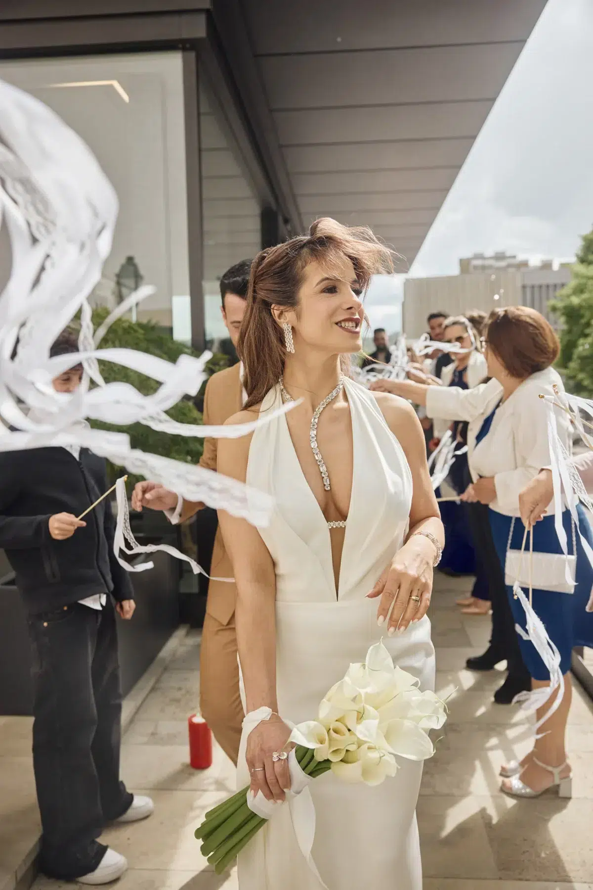 Bride and groom leaving their wedding ceremony as guests wave white ribbon wands, photographed by a documentary wedding photographer in Luxembourg.