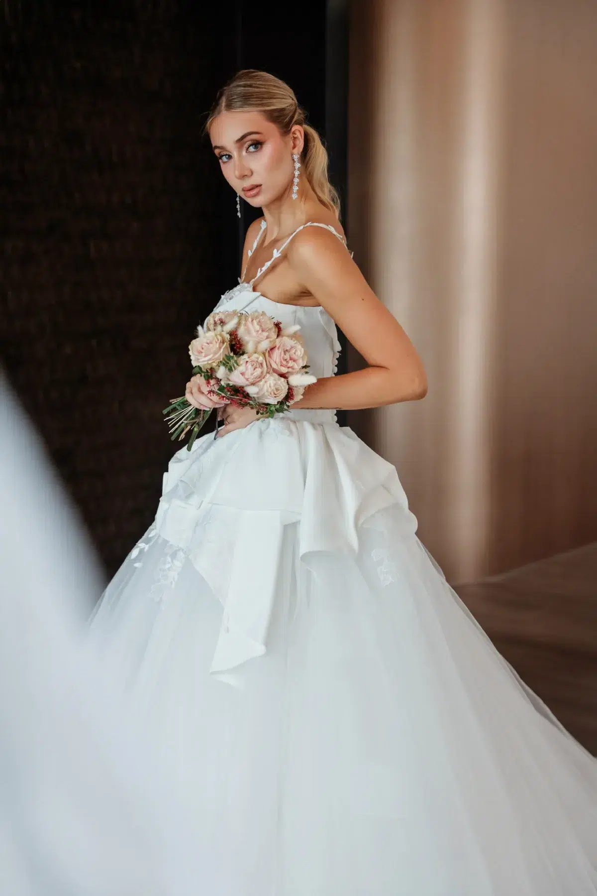 Three-quarter bridal portrait holding a blush bouquet against a dark curtain backdrop, Luxembourg wedding photography.