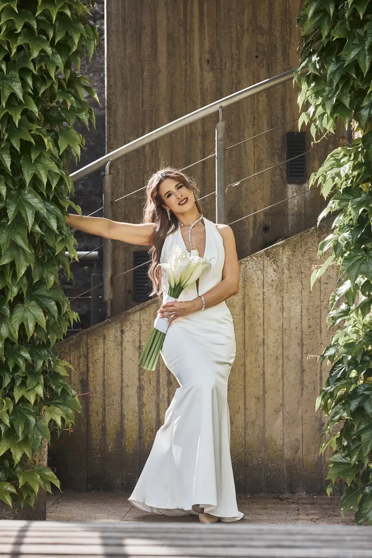 Solo bride portrait on a stone staircase surrounded by ivy, holding her calla lily bouquet, photographed in Luxembourg.