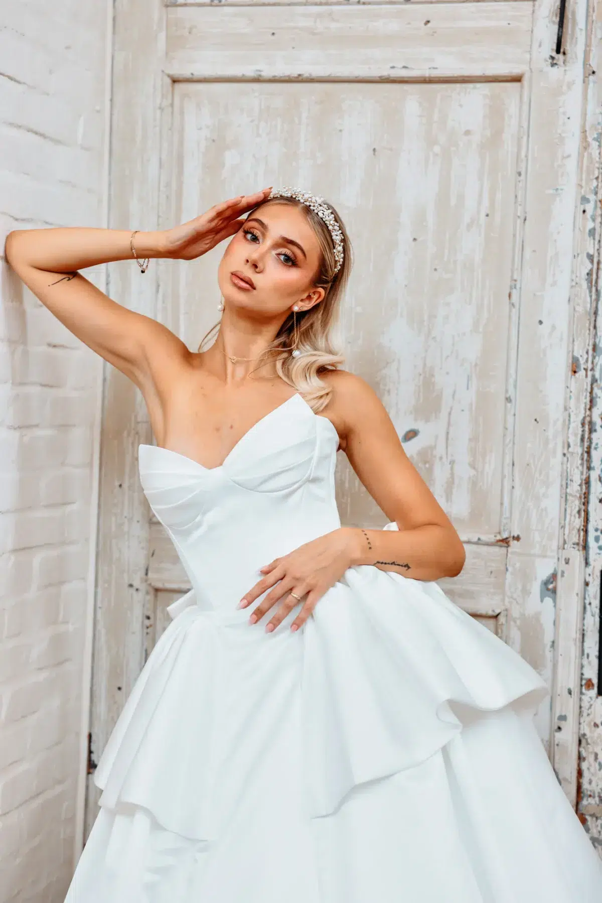 Bride wearing a pearl tiara and sweetheart bow gown poses against a weathered wooden door, bridal portrait photography in Luxembourg.