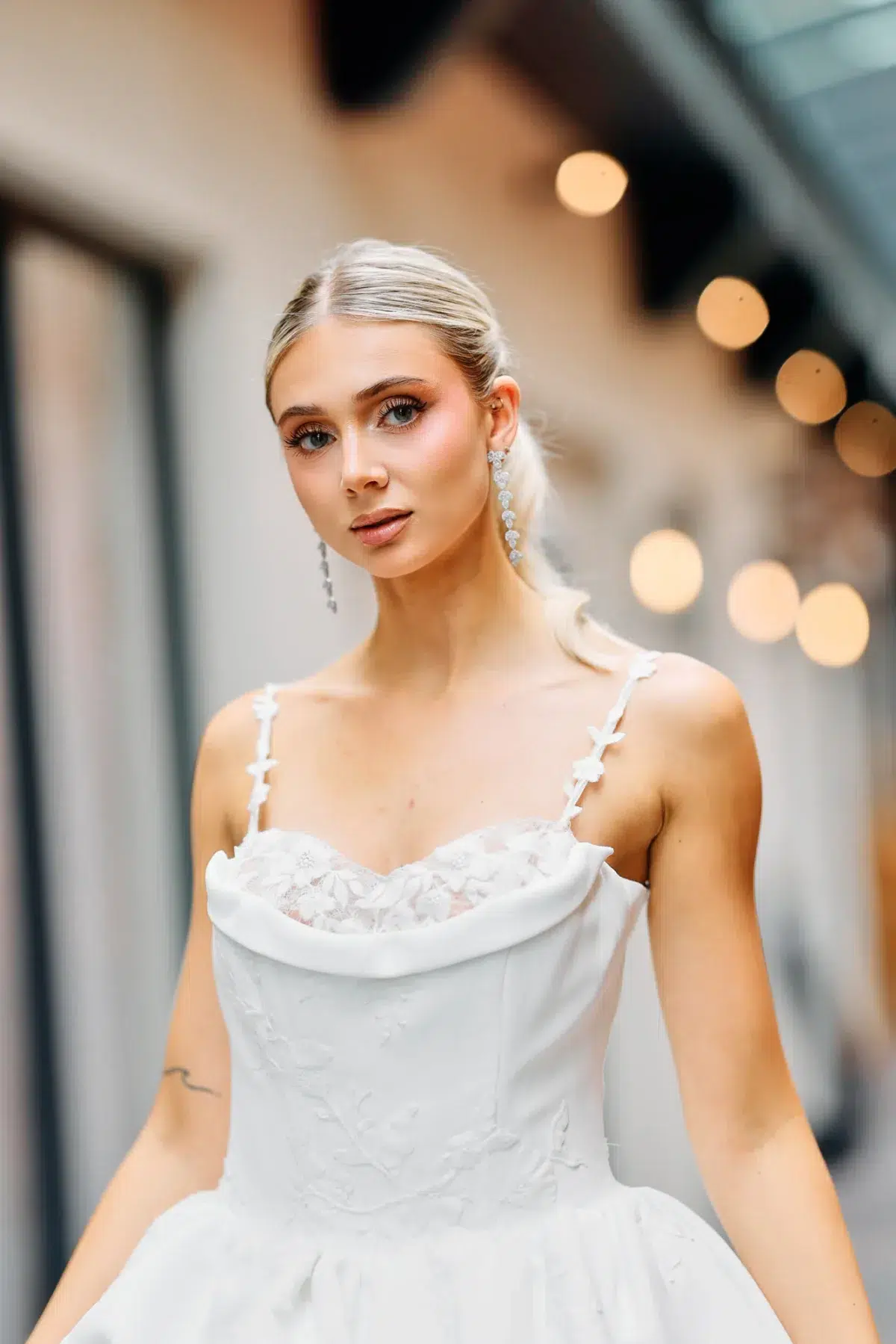 Bride in a spaghetti-strap lace ballgown photographed with soft string-light bokeh in the background, Luxembourg wedding photography.