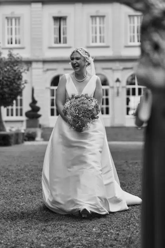 Bride laughing with her bouquet during the first look in the garden, black and white wedding photo