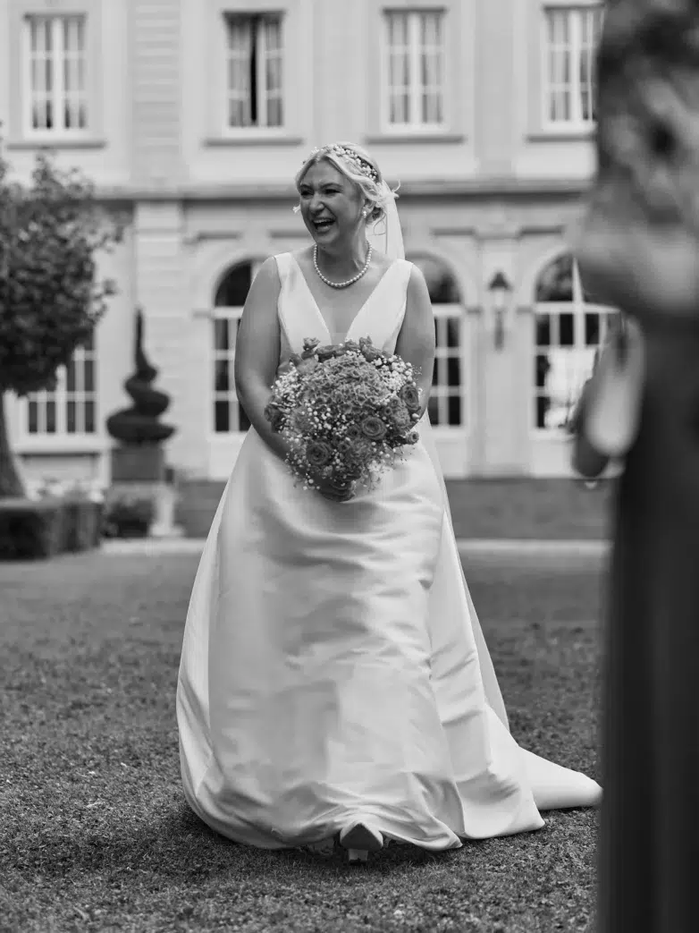 Bride laughing with her bouquet during the first look in the garden, black and white wedding photo
