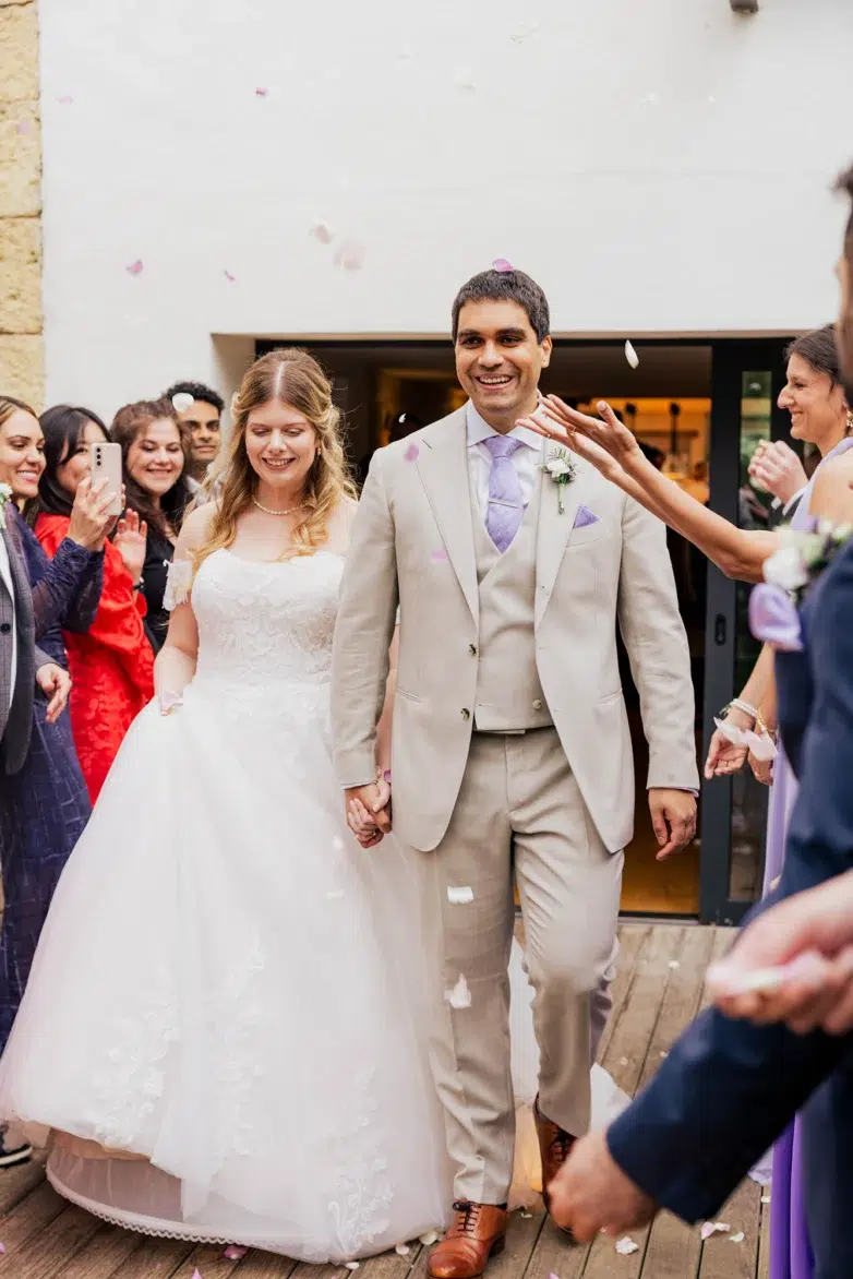 Bride and groom exiting their wedding ceremony as guests throw flower petals at Toit pour toi, Schouweiler, Luxembourg.