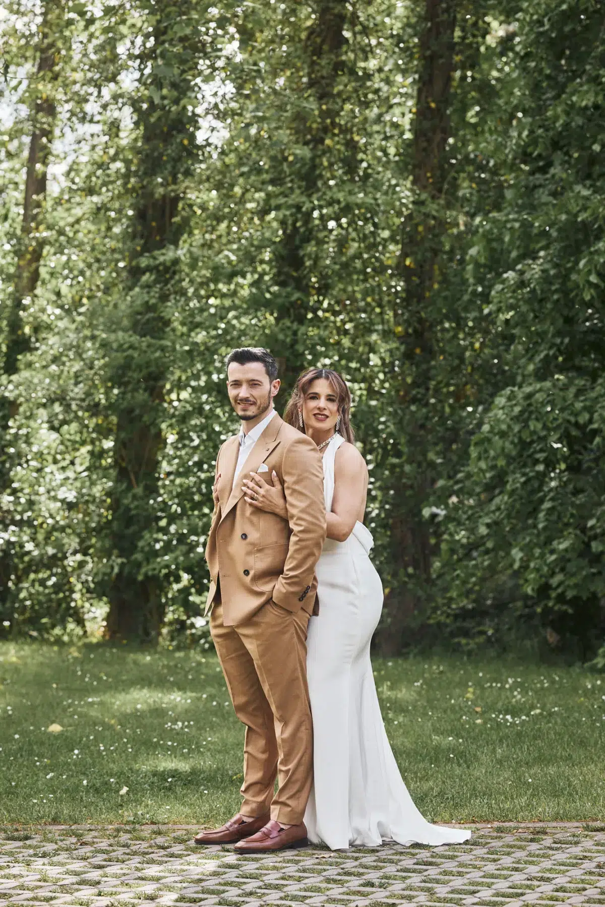 Full-length wedding portrait of a couple standing together on a tree-lined lawn, photographed during a real wedding in Luxembourg.